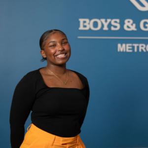 Image of Ray Ray, standing and smiling in front of a blue Boys & Girls Clubs of Metro Denver wall